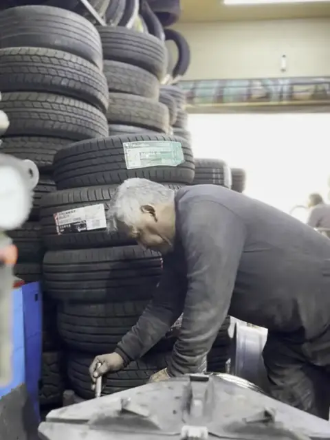 Maestro haciendo el apriete final de la rueda junto al stock de neumáticos